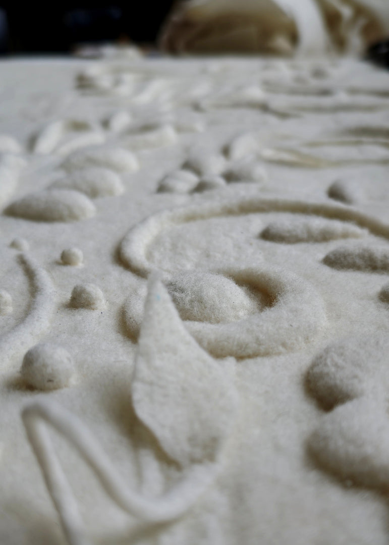 A close-up of a textured, off-white felted wool with an embossed floral and scroll pattern.