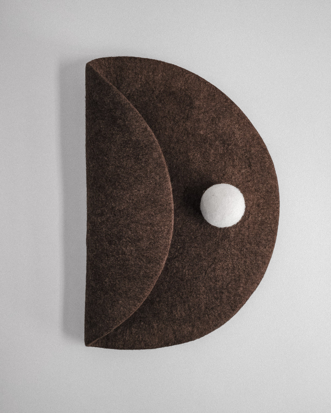 Handmade sculptural felt wall art with curved circular form and white wool sphere