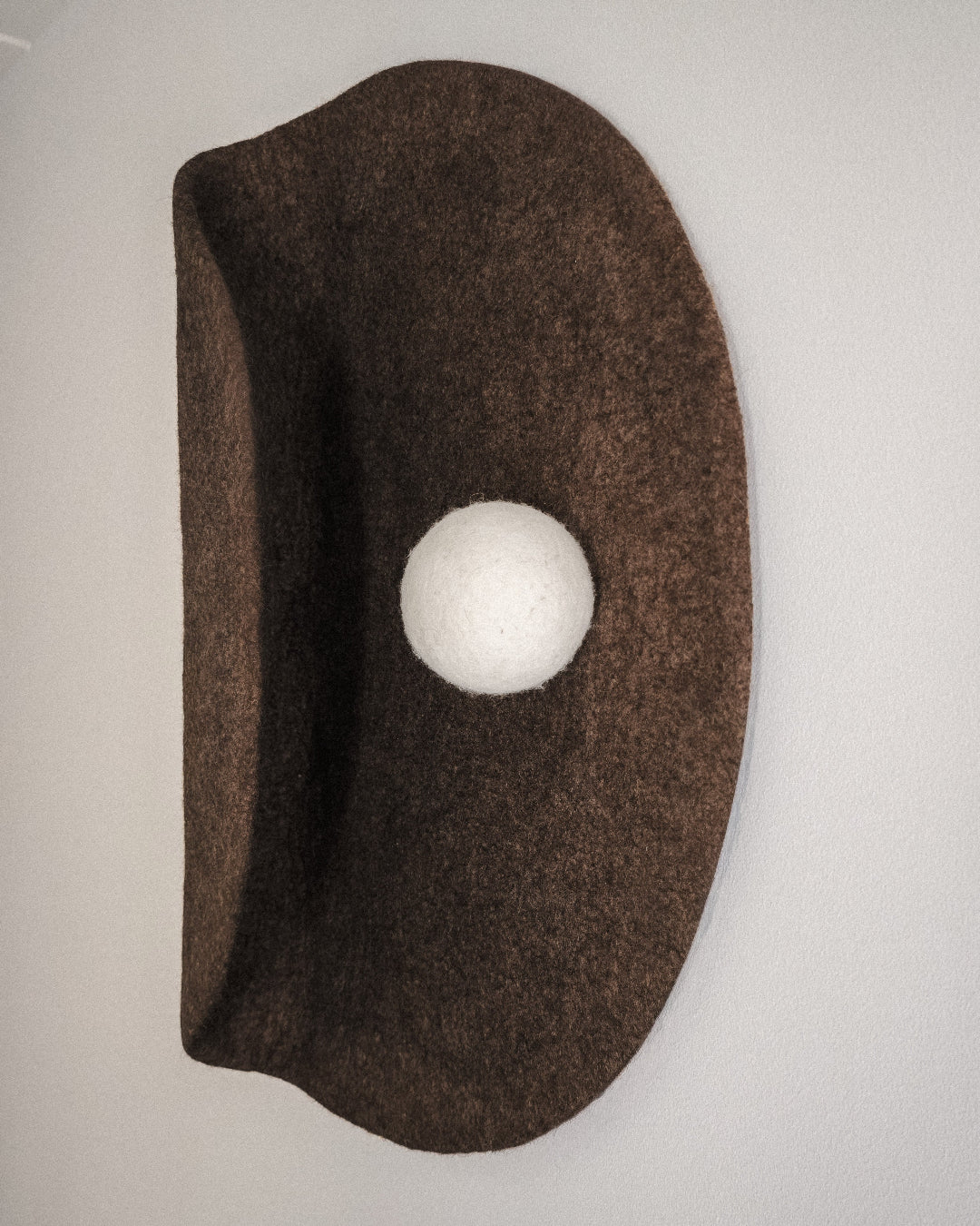 Handmade sculptural felt wall art with curved circular form and white wool sphere