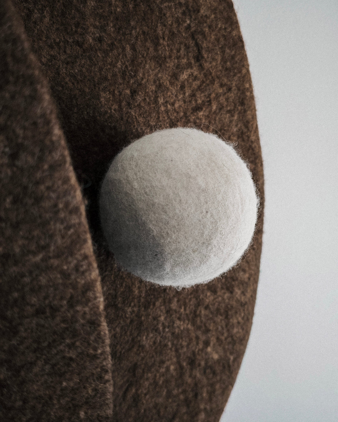 Detail of sculptural felt wall art with soft wool texture and spherical form in natural tones